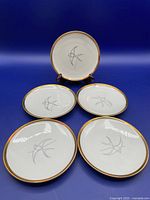 Five small porcelain dishes arranged with one propped up and four lying flat showing bird swirl designs and gold rims.