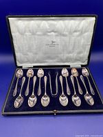 Full view of boxed set containing 12 coffee spoons and sugar tongs in navy velvet lined box with white silk lid lining stamped Walker & Hall Ltd Sheffield.