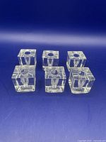 Set of six clear glass cube candlestick holders arranged in two rows on a blue background.