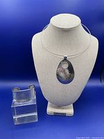 Photo shows the sterling cuff bracelet and pendant necklace displayed side by side on a blue background with the necklace on a bust form and the cuff on a clear block.