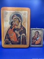 Two hand painted Madonna and Child icons against blue background showing relative size and style difference.