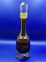Full view of amber brown crystal art glass decanter with clear glass stopper on blue background