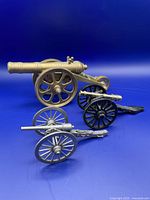 Three miniature cannons in brass, cast iron, and pewter lined up on blue background.