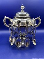 Silver plate spooner with handles, lid removed in second image. Twelve silver plate tea spoons with Queen Mary pattern hang on spooner rack.