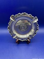 Front view of round sterling silver ashtray with scalloped edges and four cigarette rests.