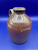 Front side of small brown stoneware jug showing embossed 'Perth' and speckled glaze texture.