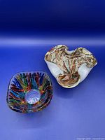 Two Murano glass bowls shown on a blue background. One is a colorful square bowl; the other is an organic-shaped bowl with mixed colors and gold flecks.