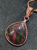 Close-up front view of teardrop-shaped enhanced opal pendant set in 14K gold with visible colorful flashes under lighting.