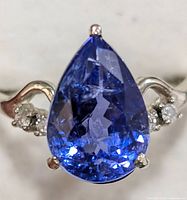 Close-up top view of pear-cut violet-blue tanzanite center with white gold prongs and round-cut accent stones on shoulders