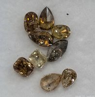 Ten loose fancy color diamonds in assorted shapes and colors arranged on white surface