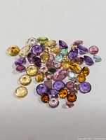 Loose assorted genuine gemstones displayed on a white surface showing various colors and cuts.