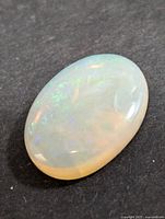 Close-up image of oval polished Australian opal with visible play-of-color on a dark background taken to show gemstone quality and colors.