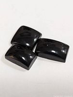 Three polished black onyx cabochon gemstones arranged on a white surface, showing shiny curved tops and smooth surfaces.