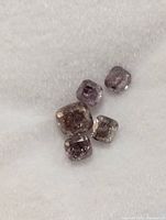 Five cushion-shaped rough pink diamonds on white foam pad