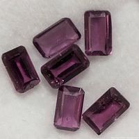 Six rectangular cut reddish-purple garnet stones on white background.