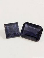Two genuine iolite gemstones placed on white background, showing color and cut details under light.