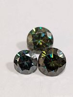 Three round genuine moissanite stones on white background showing multiple color reflections and facets