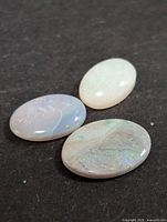 Three oval-shaped genuine opal gemstones on a dark surface showing their colors and textures