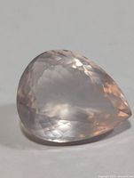 Close-up images of a single pear-shaped rose quartz gemstone, showing multiple faceted cuts and polished surfaces. The gemstone is translucent pink and displays light reflections.