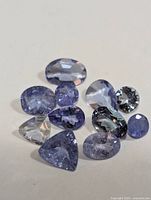 Multiple loose tanzanite gemstones in various cuts and sizes on a white background to show diversity and color.