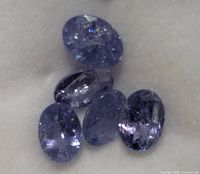 Five oval cut tanzanite gemstones on white felt showing color and inclusions.