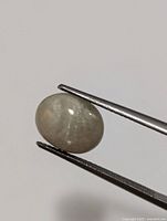 Zultanite gemstone held by tweezers against a plain background, showing smooth polished cabochon shape.