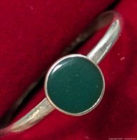 Close-up of silver ring with round green stone on red background