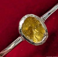 Close-up view of silver ring with visible yellow stone and bezel setting against red background