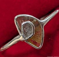 Close-up front view of the silver ring showing the diamond and the geometric setting against a red background.