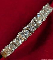 Close-up image showing the clear round stones set in the silver band on a red background, focusing on the prong settings and stone alignment.