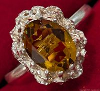 Close-up front angle of the silver ring with yellow faceted gemstone on a red background showing stone and decorative setting detail.