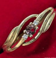 Close-up image of silver ring showing twisted band design, central oval purple stone and two small clear stones on each side against red background.