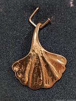 Silver ginkgo leaf pendant front view on dark background showing curving shape and vein textures.