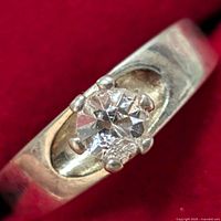 Close-up of silver ring showing clear faceted gemstone in prong setting on polished band.