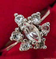 Close-up front view of silver ring with central marquise-cut clear stone and surrounding round clear stones in cluster.