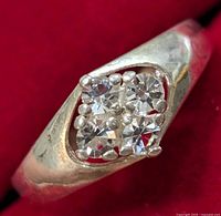 Close-up photo showing the front angle of the silver ring with four clear stones set in a square cluster, against a red background.
