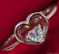 Close-up image of a sterling silver ring featuring an open heart design with a heart-shaped cubic zirconia centerpiece, showing detail and condition of the ring.