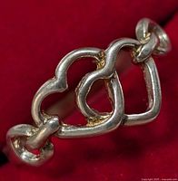 Close-up image of the silver ring showing the two interlocking heart shapes linked together, placed on a red background.