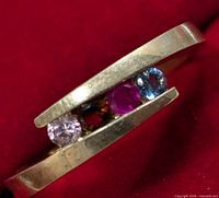 Close-up of silver ring with four different colored stones set in a split band design on a red background.