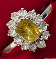 Close-up front view of the ring showing central yellow gem surrounded by diamonds in silver setting.
