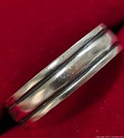 Close-up image of a sterling silver ring on a red background showing the grooved band detail and polished surface with slight wear.