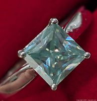 Close-up of the ring showing the square princess-cut moissanite stone with visible facets, set in a silver band.