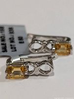 Close-up image of one silver earring with rectangular step-cut citrine gemstone and infinity design in polished silver marked 925.
