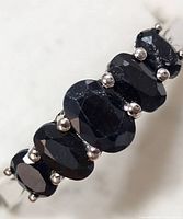 Close-up front view of the silver ring showing five dark faceted sapphire stones.