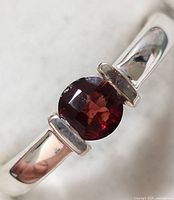 Close-up photo of the sterling silver ring with central oval garnet gemstone showing polished finish and gemstone facets.