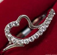 Close-up photo of silver heart-shaped ring set with clear round cubic zirconia stones on a red background.