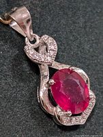 Close-up of the front side of the silver pendant featuring an oval red ruby gemstone and clear accent stones on its setting.