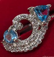 Close-up photo of silver ring with blue topaz stones and clear accent stones in a swirling design on red background