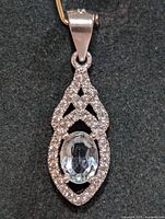 Front view of silver pendant with blue topaz center stone and surrounding cubic zirconia set in decorative lattice design.