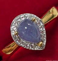 Close-up of sterling silver ring featuring a pear-shaped tanzanite gemstone with clear cubic zirconia stones surrounding it, displayed on a red background.